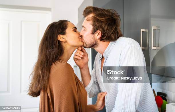 Young Woman Kissing Her Boyfriend In Their Kitchen Stock Photo - Download Image Now - Couple - Relationship, Face To Face, Romance
