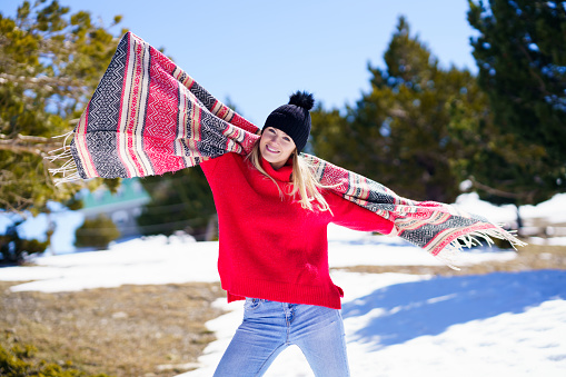 Happy young blonde woman waving her scarf in the wind in a forest in the snowy mountains in Sierra Nevada, Granada, Andalusia, Spain