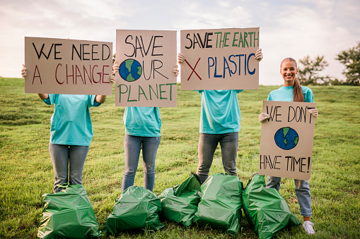 Group of happy volunteers holding paperboard with inscription after cleaning nature area from the trash. People are holding banner signs while they are going to a demonstration against climate change. Protest against global warming. Climate change protest concept.