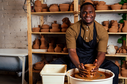 happy dark-skinned african american businessman potter man molding In workshop. sculptor pottering clay pot in a studio workplace. creativity and inspiration of the artist