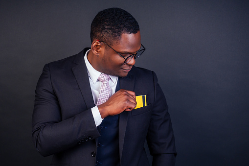 young successful businessman man in a stylish black classic suit and in cool glasses holding a yellow plastic credit card in the studio on a dark background. shopping concept