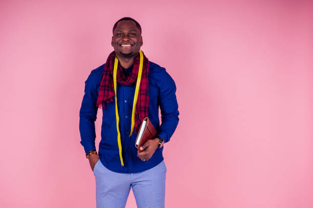 istock African American man working in a tailor seamstress workshop stylish male model clothes designer with a measuring tape on the neck posing on a pink background in the studio 1425296300