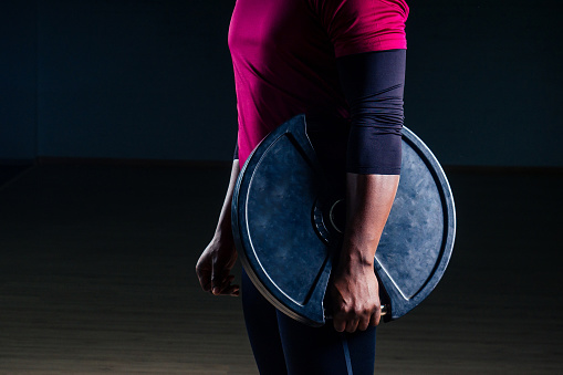 muscular shirtless young african american man in sportswear tire exercising with tyre in gym on a black background in the studio workshop