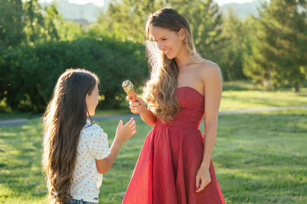 schöne langhaarige kleine mädchen tochter zahnig lächeln lange haare und mutter isst pistazieneis im park hitze sommerreise. jugend- und frischekonzept - offspring child toothy smile beautiful stock-fotos und bilder