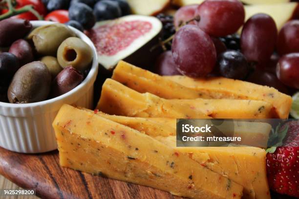 Closeup Image Of Wooden Charcuterie Board Rows Of Chilli Cheddar Cheese Triangles Red Grapes Strawberries Blackberries Figs Red Vine Tomatoes Apple Blueberries Ramekin Of Green And Black Olives Focus On Foreground Stock Photo - Download Image Now