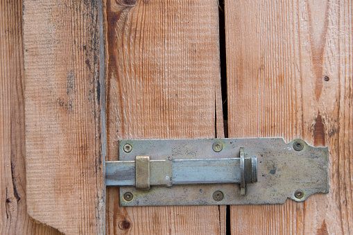 Close up of wooden door made of boards with metal brass iron locking bar lock as a concept for locked storage rooms