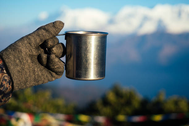 una taza de metal con una bebida caliente en la mano contra el fondo de las montañas. el concepto de unas vacaciones activas en las montañas. tourizm en temporada de frío - texas tea fotografías e imágenes de stock