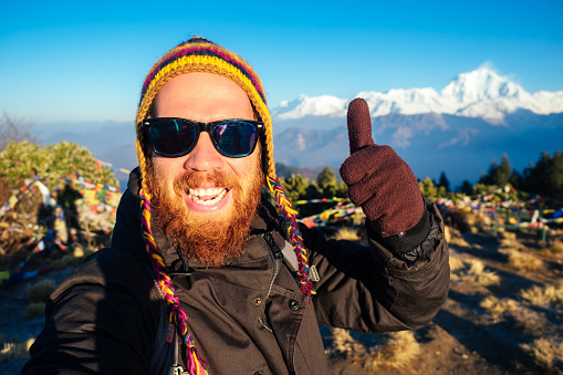 A young man with a red beard and a backpack in the mountains makes a selfie. the concept of active recreation and tourism in the mountains. Nepal in the spring.