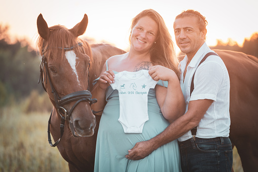 Pregnant woman and her husband are enjoying the happiness of their newborn children with their horses