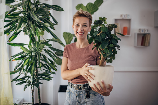One woman, portrait of a beautiful shorthaired woman holding a houseplant at home.