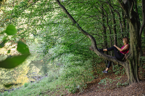 Sporty woman sitting on a tree branch enjoying the view of nature