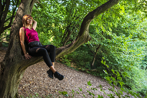 Sporty woman sitting on a tree branch enjoying the view of nature