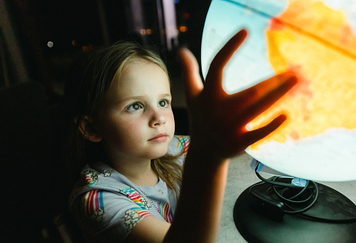 Little girl looking at globe lamp in the dark room at night