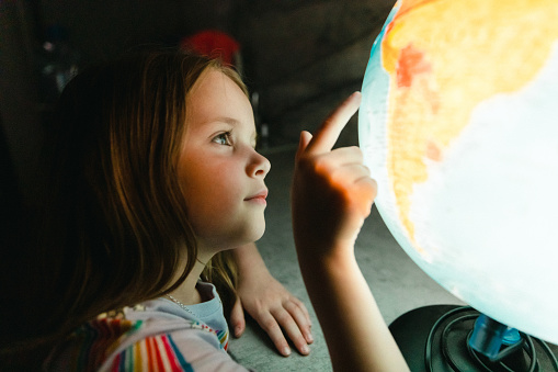 Little girl looking at globe lamp in the dark room at night
