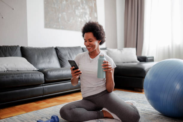 istock Mature black woman using her smart phone while refreshment with water after intensive home workout 1425310715