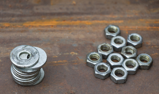 A few flat metal washers and Metal shine nuts in te background on a on a metal surface.
