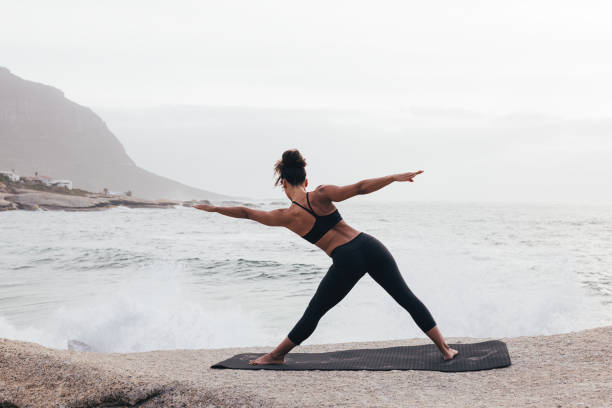 istock Back view of fit woman doing warming up exercises on mat by ocean 1425336511