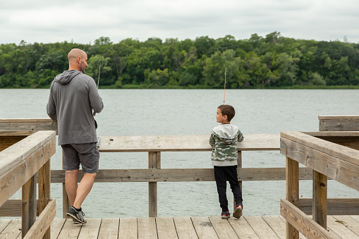 Rear view of a father and son fishing from a wooden dock at a small lake.