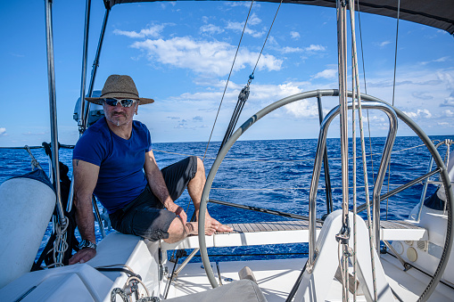 A man wearing a straw hat  is driving a sailboat and enjoying it.
