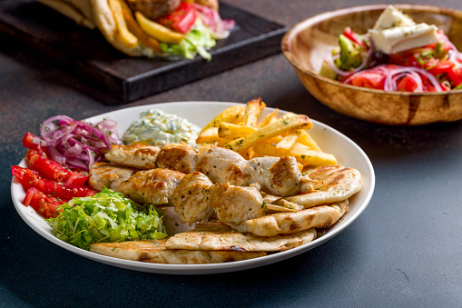 souvlaki with chicken vegetables and pita, greek salad with feta and pita gyros with beef patty and vegetable on dark stone table, selective focus, macro close up