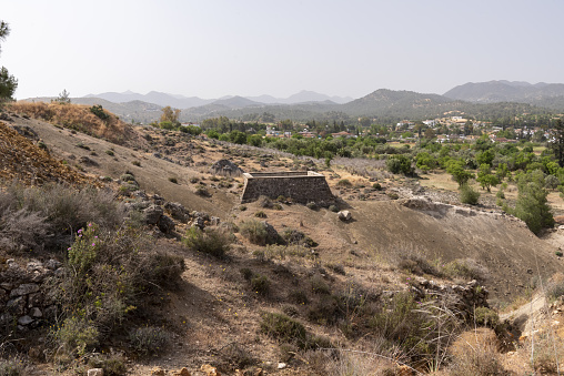 Water cistern at historic gold processing site on arid hillside with village and mountain range in the background