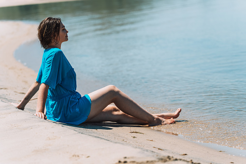 Girl in a blue pareo sitting on the beach against river.