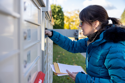 A woman is collecting post at home in autumn, Quebec, Canada. She is smiling and unlocking the mailbox. She is pickup-up her mail and looking at the letters she received.