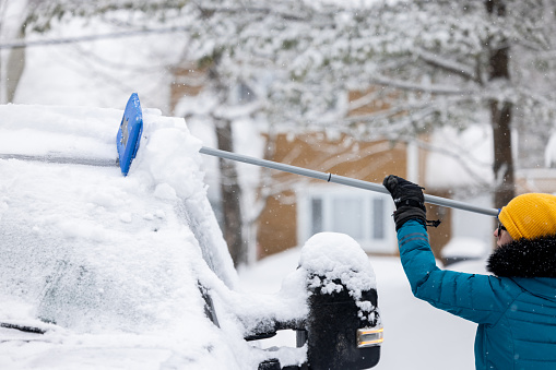 Young woman cleaning snow off her car after snowstorm