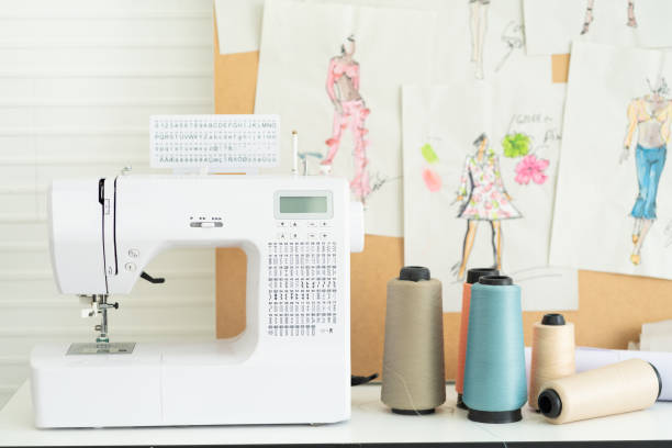 máquina de costura e multicoloração de rosca na mesa na alfaiataria. moda, conceito de costureira - sewing machine sewing sewing item needle - fotografias e filmes do acervo