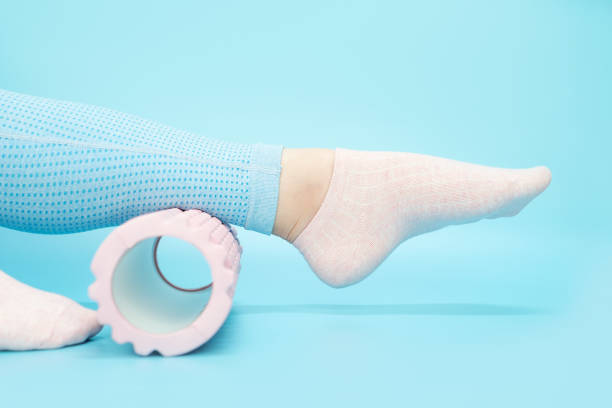 istock Female leg rolls a massage foam roller close-up on blue background, side view. 1425395841