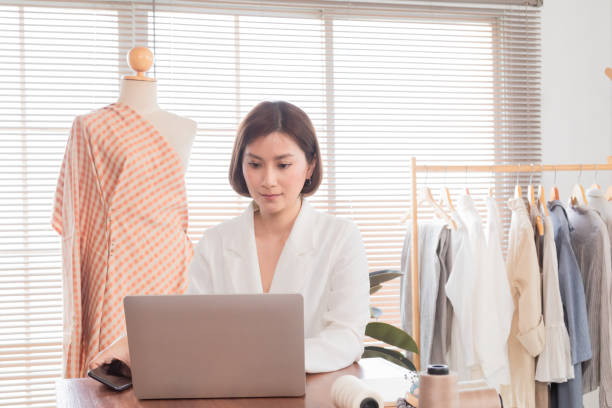 istock Beautiful Asian working woman using laptop working on studio, Young businesswoman work professional design clothes to sell online in workshop. Owners taking orders online while work from home. 1425397595