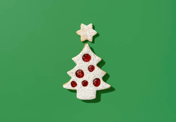 Christmas tree shaped cookie on a green background, top view Above view with a cookie shaped like a christmas tree and a star. Delicious linzer cookies with raspberry jam, minimalist on a green table. Christmas Tree Cookie stock pictures, royalty-free photos & images