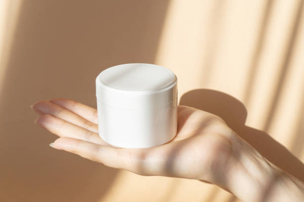 mockup of white package with cream stands on palm of woman. unmarked container for gel, shampoo in sunlight on beige background. concept of body care, beauty industry - moisturizer cosmetics merchandise human hand imagens e fotografias de stock