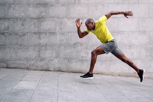 Side view of an african American sportsman with yellow t-shirt and shorts sprinting up on inclined floor and concrete wall behind outdoors.