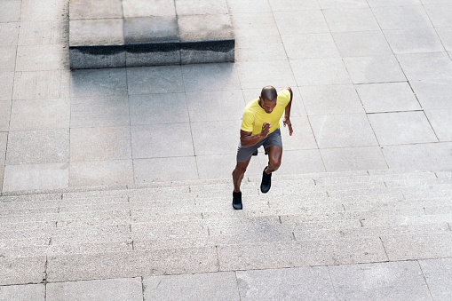 Aerial view of an African American sportsman with yellow t-shirt and shorts sprinting up on stairs outdoors.