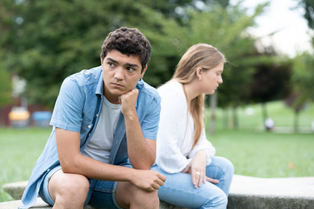 Pensive sad hispanic boy thinking on couple relationship Pensive and sad hispanic boy thinking on couple relationship sitting back to back with girlfriend outdoors in a park teenager couple child blond hair stock pictures, royalty-free photos & images