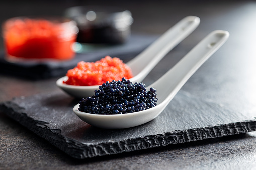 Red and black caviar in ceramic spoon on the dark table.