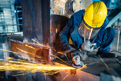 Metal polishing with a hand sander with a polishing disk. Clip. Factory worker at workshop grinding steel rod with abrasive disc and flying sparks. Hand grinder workflow creation stainless pipe. working process with the sparks.