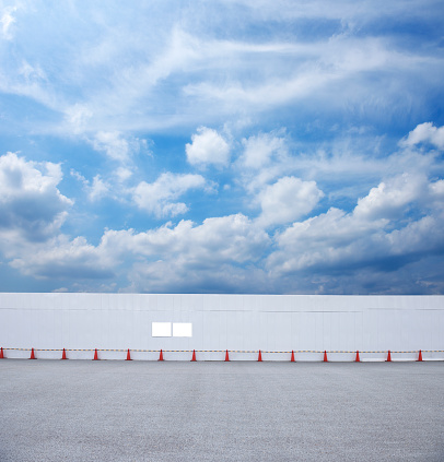 Long metal white wall panels at construction site with red traffic corn, against blue sky with cloudscape.