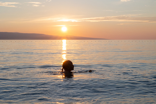 Little girl learns to swim in the sea. The sun sets over the horizon. Sunlight reflects on the surface of the sea water. Adriatic Sea. Croatia.