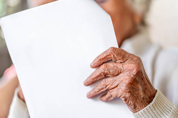 Close-up of hand, old woman with wrinkled hands reading a white letter stock photo