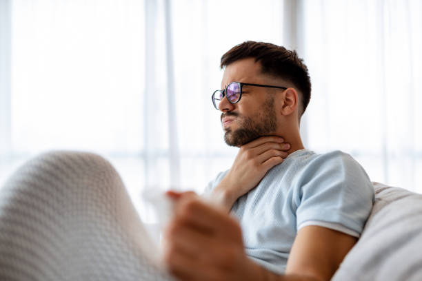 Sick man lying on the couch with high temperature and holding his throat with hand. Sick man lying on the couch with high temperature and holding his throat with hand. sore throat stock pictures, royalty-free photos & images