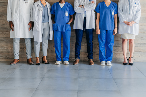 Team of professional, medical coworkers, against wood background, together show diversity, in hospital corridor. Group of doctors and nurses, against brown backdrop, in clinic or healthcare facility.