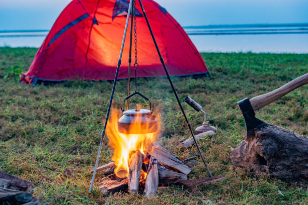 istock Campfire in orange tent camping on grass by lake 1425430612