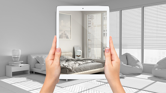Hands holding tablet showing modern bedroom and lounge, total blank project background, augmented reality concept, application to simulate furniture and interior design products