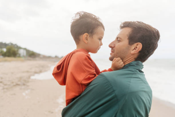Photo of a little boy and his dad sharing some affection and love at the beach during sea storm
