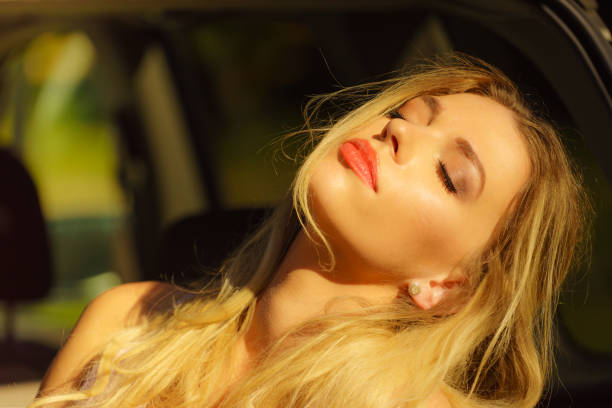 Young beautiful blonde woman relaxing in car during summer vacations trip. Moment of chillout while traveling.