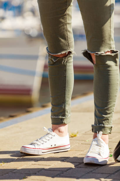 Legs wearing trousers and sneakers Trendy fashionable unrecognizable female relaxing outdoor wearing casual footwear white sneakers and hole trousers. hole in pants stock pictures, royalty-free photos & images