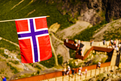 Trollstigen mountain road landscape in Norway, Europe. Norwegian flag waving and many tourists people on viewing platform in background. National tourist route.
