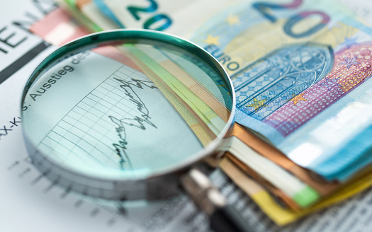 a magnifying glass lies on a stock exchange info, next to it a pile of euro banknotes as a symbol for profits. this photo was taken with a professional camera and lens with raw processing for best quality with an open aperture for smooth transitions and focus on the essentials. Concept for: financial development, bank account, statistics, investment Analytical research data economy, stock market trading